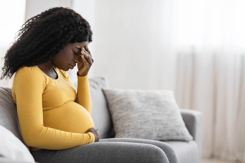 Pregnant woman sitting down and holding a hand to her head